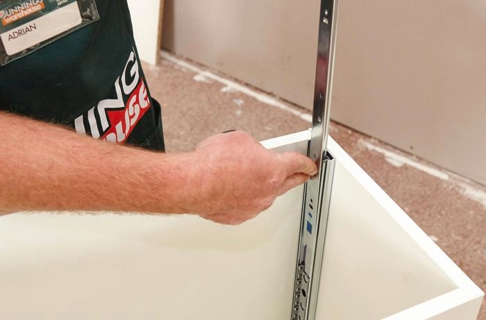 Person attaching drawer runners to inside of cabinet