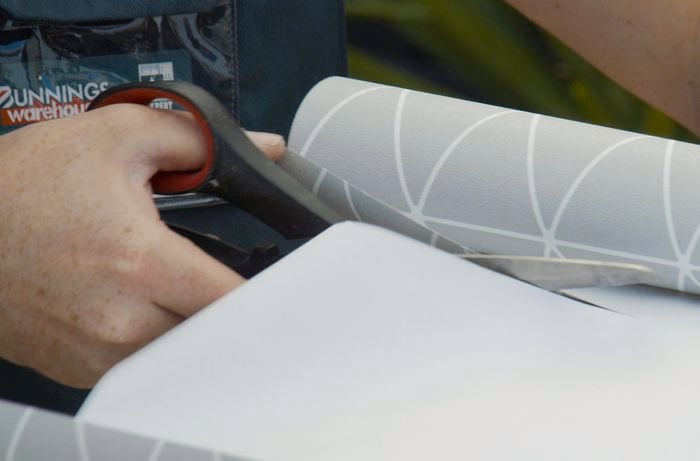 Person cutting a roll of wallpaper with scissors