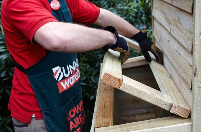 A wooden access hatch being built into the side of a chicken coop by a Bunnings team member