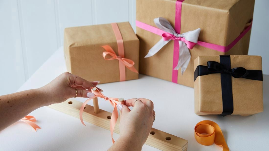 Person with a finished bow made using the bow maker and gift boxes with bows. 