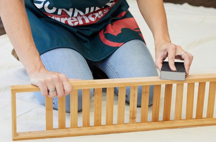 A woman uses a sanding sponge to lightly smooth over a timber bath caddy to prepare for painting.