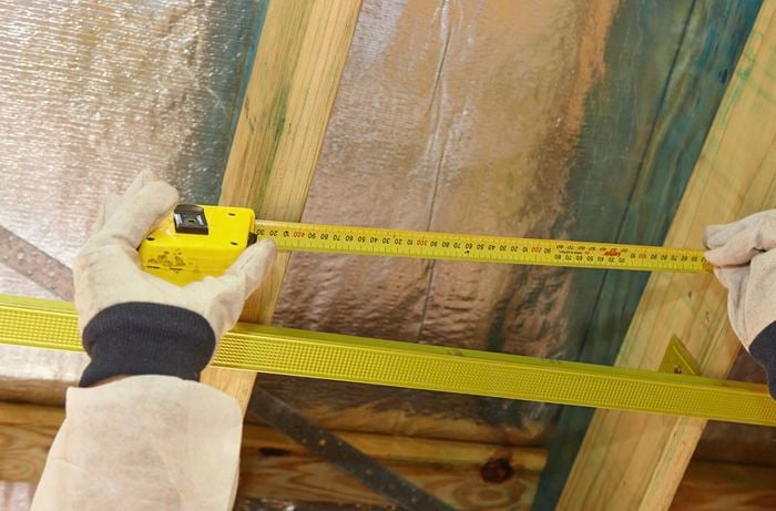 A person measuring the distance between joists in a ceiling