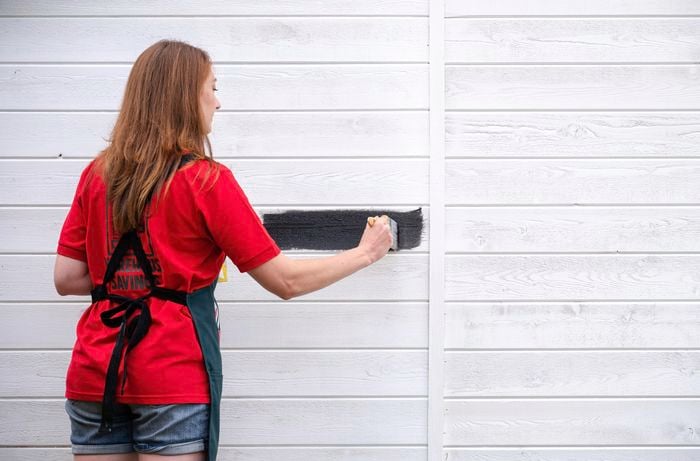 A Bunnings team member painting the exterior of a shed after having applied an undercoat