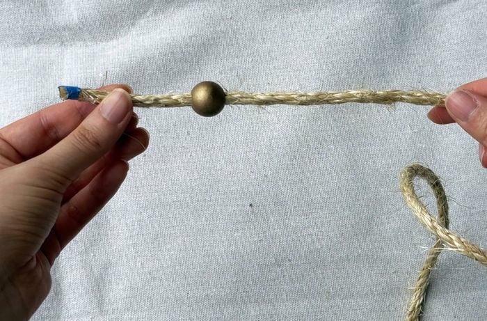  A pair of hands holds some twine with a gold bead threaded on it, on a drop sheet.