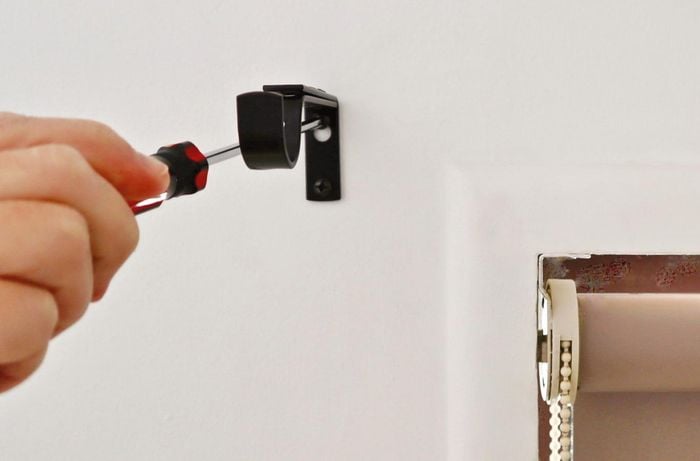 A person screws curtain rod brackets into wall