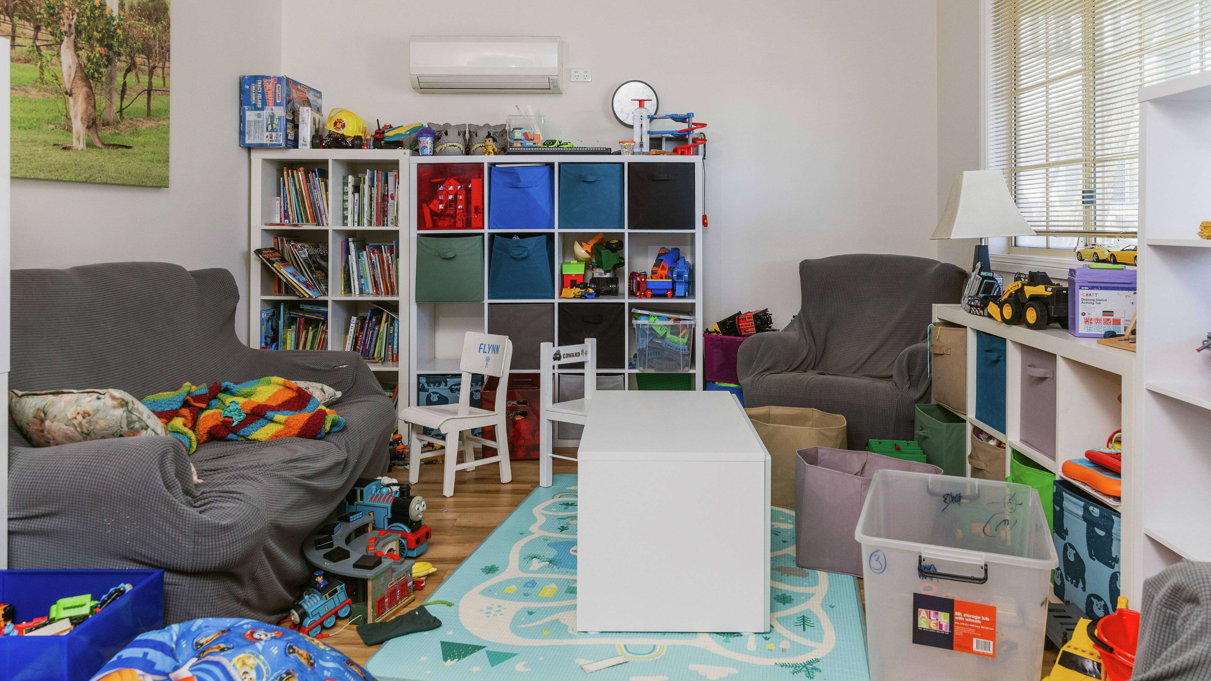 Tidy playroom featuring blue-and-white storage cubbies, neatly arranged toys, and sunlight filtering through a large window.