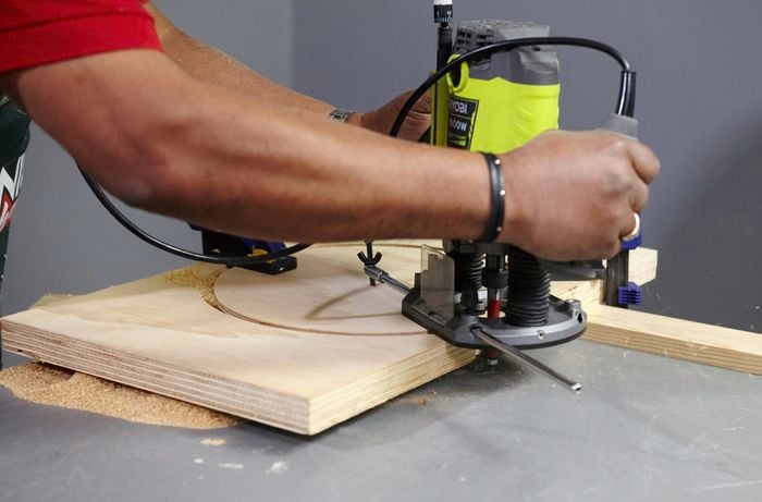 A circular stool seat being cut from a square wooden panel with a router