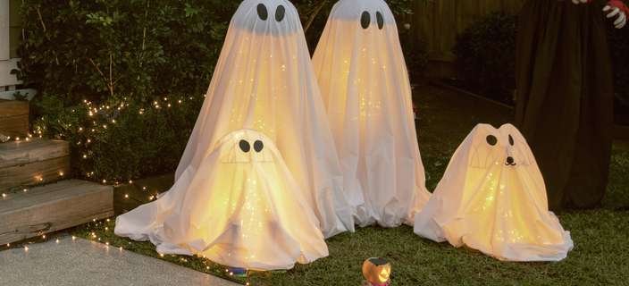Halloween ghost decorations in a garden at night, surrounded by fairy lights.