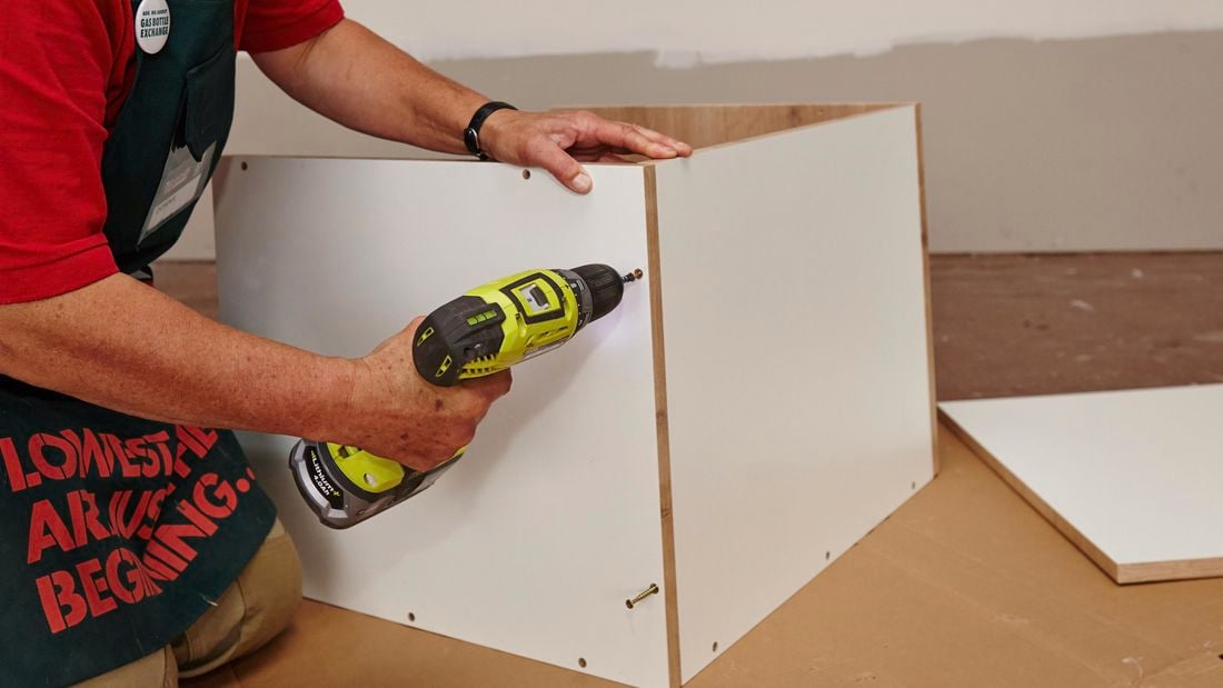 A person assembling a cabinet using a cordless driver