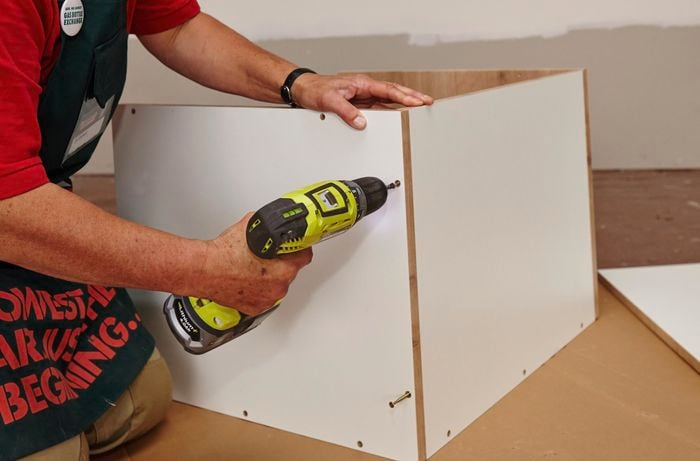 A person assembling a cabinet using a cordless driver