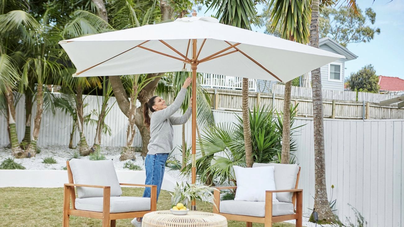 A white market umbrella covers two cushioned outdoor armchairs