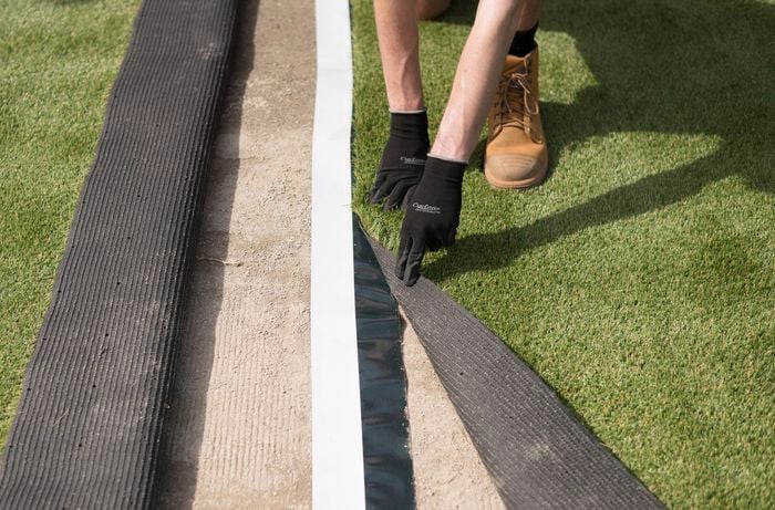 A person wearing gloves is aligning two sections of synthetic turf over adhesive tape to join them seamlessly.
