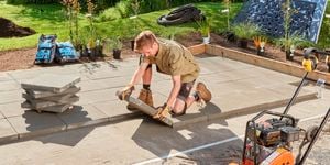 A landscaper laying pavers in a backyard with lawn and plants.
