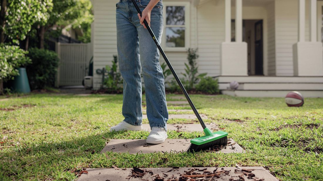 A person wearing jeans sweeping an outdoor garden path with an Oates broom