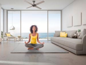 A woman meditating underneath a ceiling fan in a room overlooking the ocean