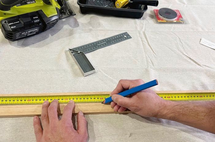  A left hand holds a tape measure in place over a piece of timber while the other marks the timber with a pencil