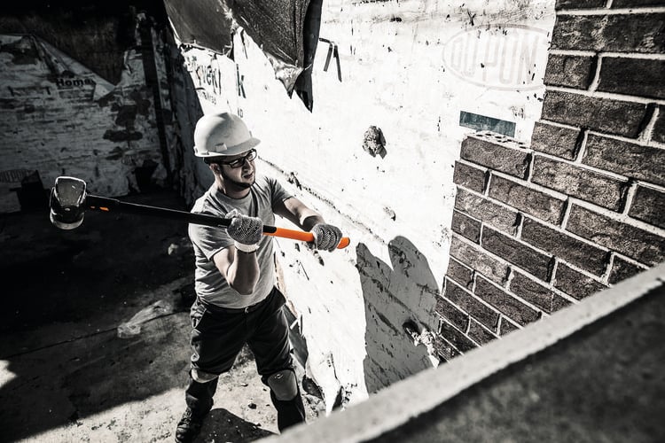 A tradesman dismantling a brick wall with a sledgehammer
