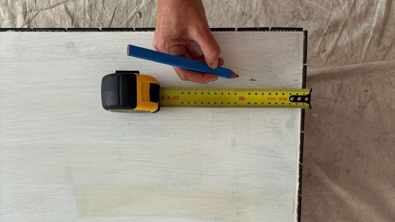 A hand marking the table top using a tape measure and a pencil.