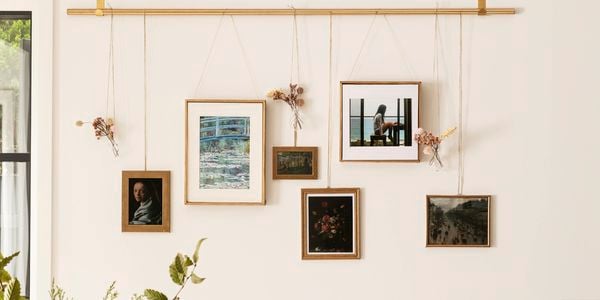 D.I.Y. hanging artworks and floral arrangements designed as a gallery wall from a gold rod on a cream wall behind a table