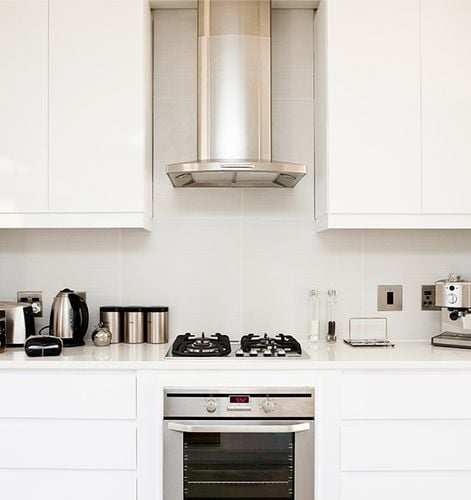 Oven, cooktop and rangehood surrounded by white kitchen cabinets and benchtops