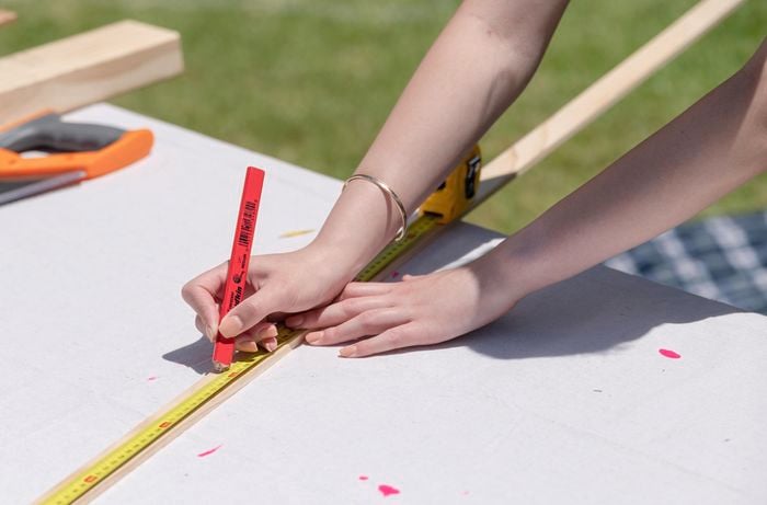 Person marking up timber using tape measure and pencil.