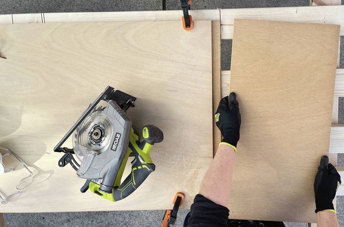 Hands in black gloves holding a piece of plywood next to a circular saw. [[2609] MAK...me sign_V1 | Word]
