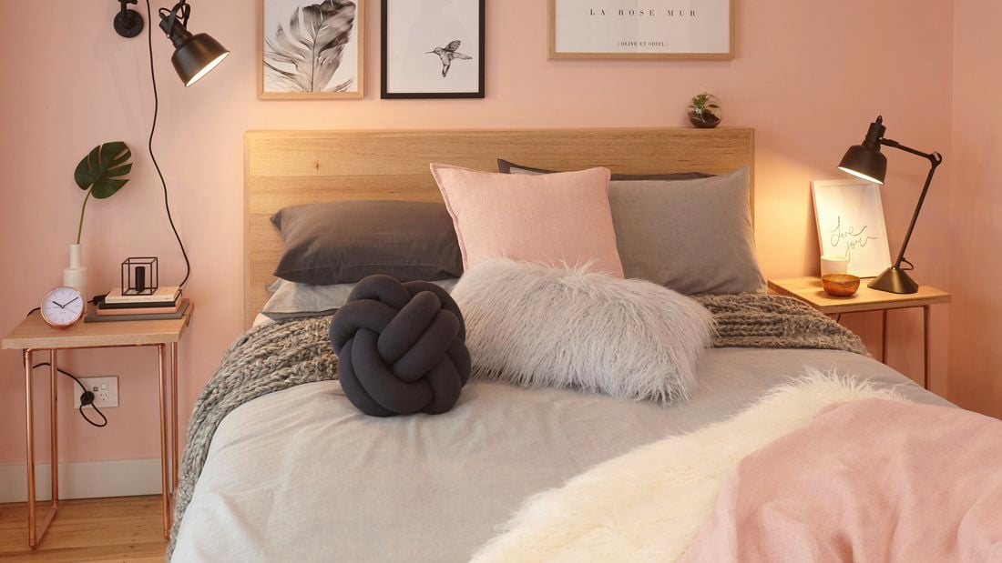 Bed with timber bedhead and many decorative pillows.