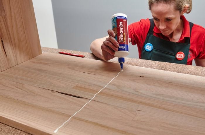 A person applying glue in a line across a timber panel