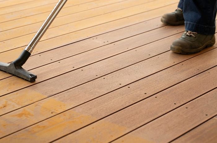 A person is using vacuum to to remove fine sanding dust from a timber deck between each sanding stage.​ 