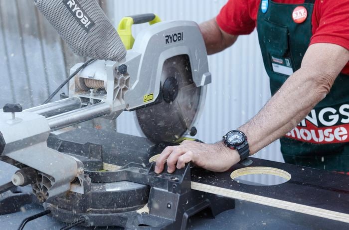 A circular saw cutting through a piece of particle board painted black with a hole in the centre