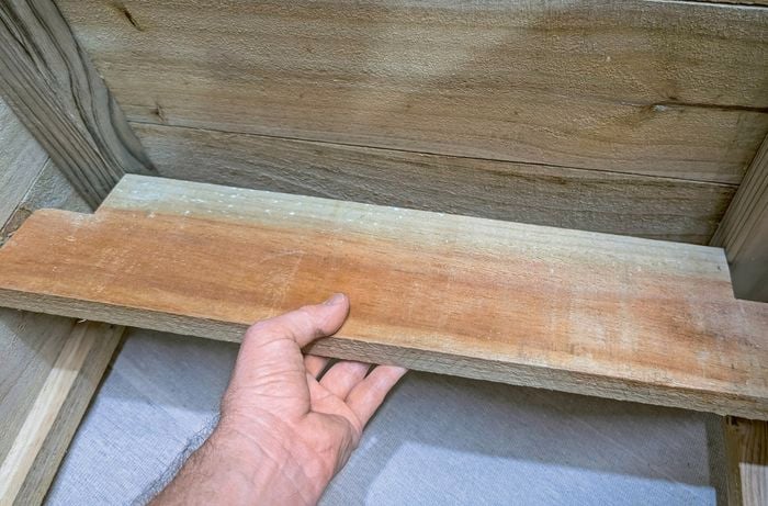 Hands reinforcing the inside of a wooden planter box with a notched timber base piece.