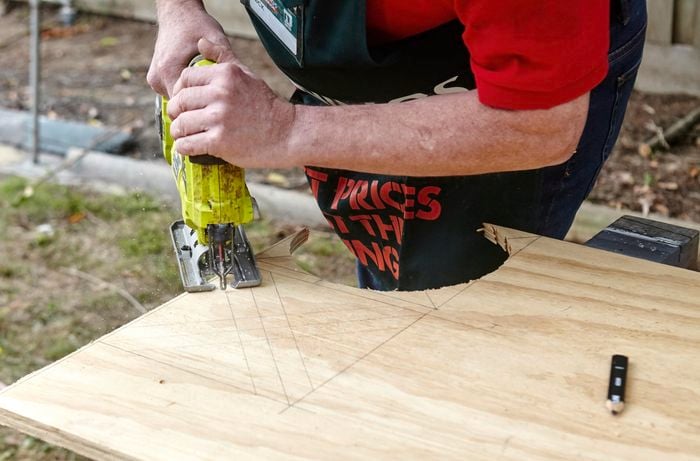 A person cutting a sheet of plywood using a jigsaw