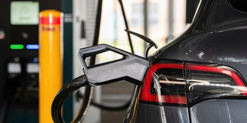 A close-up view of an electric vehicle charging connector plugged into the rear of a Tesla at a fast-charging station_.png