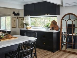 A rustic themed kitchen with black cabinets, marble countertop and wooden trim