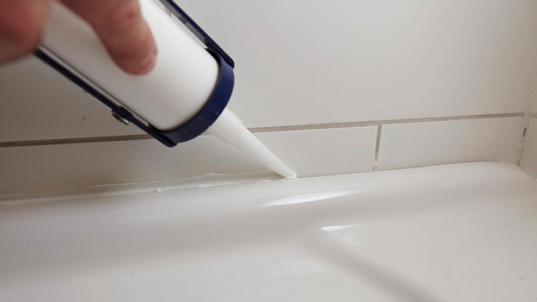Person using caulking gun to silicone gap between bath tub and wall.