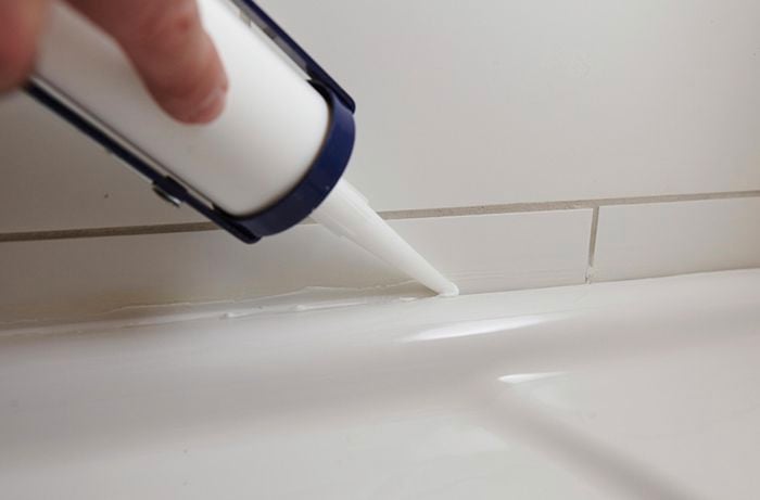 Person using caulking gun to silicone gap between bath tub and wall.