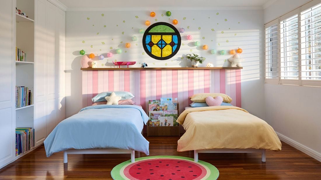 Two single beds in a Bluey-inspired bedroom with a watermelon rug, stained glass window, lanterns and pink bedhead panelling