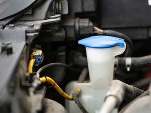 A car’s windshield washer fluid reservoir is shown with its blue cap closed.
