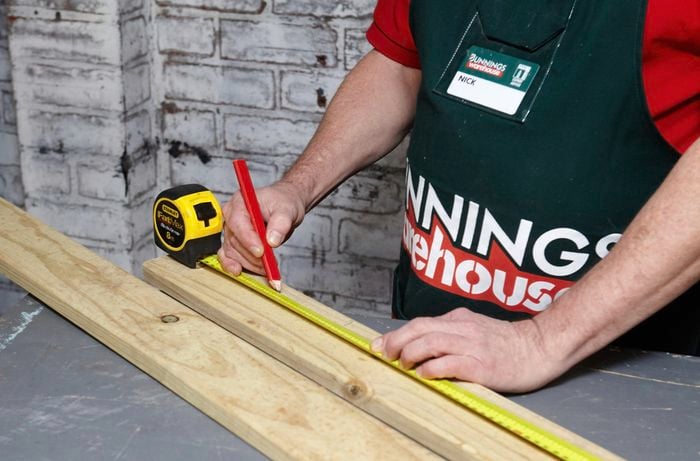 A pencil and tape measure being used to mark a piece of timber for cutting