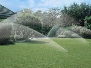 The backyard of a home showing lush green grass with five working irrigation sprinklers
