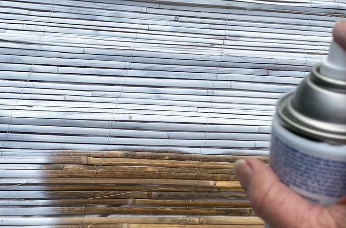 A close up of a hand using white spray paint to upcycle a bamboo screen.