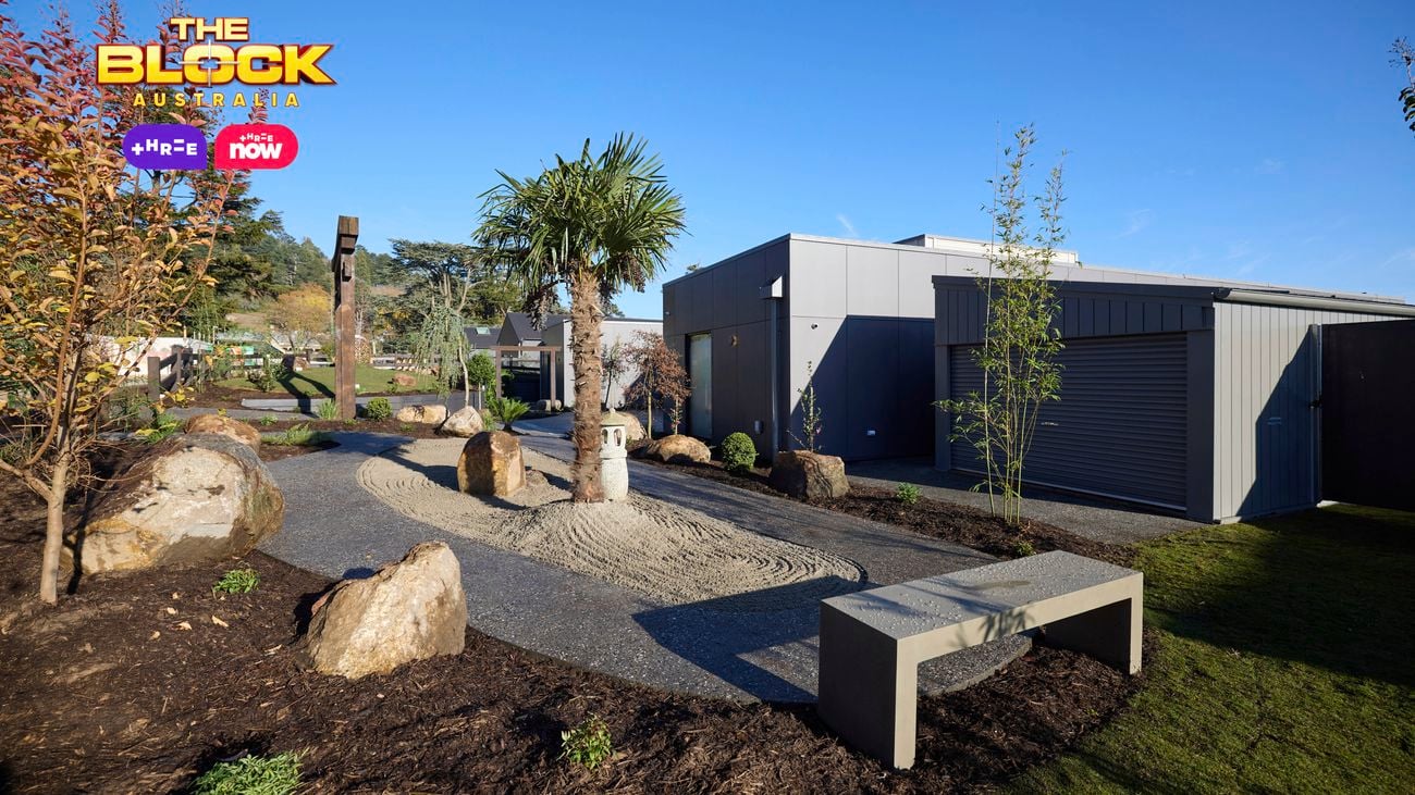 The front area of a house with a bench seat, rocks, grassed area and trees in it.