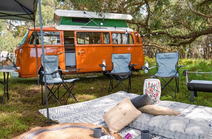 Orange combi van with camp chairs, outdoor cushions and rugs.