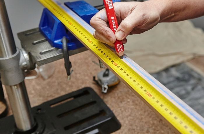 Person using measuring tape and pencil to mark up sides of wooden ladder.