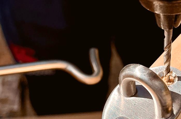A person using a drill to screw in a cabin hook to the side of a wooden panel
