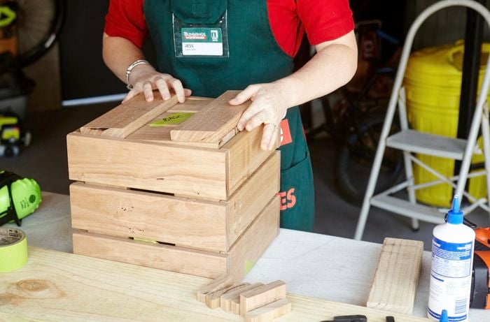 A person attaching two lengths of timber to the bottom of a planter