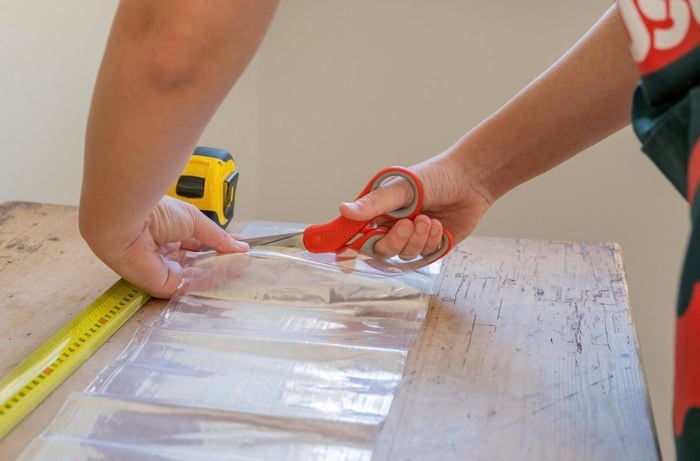 A Bunnings Team Member cutting plastic with a pair of scissor and a tape measure is next to the plastic on a table
