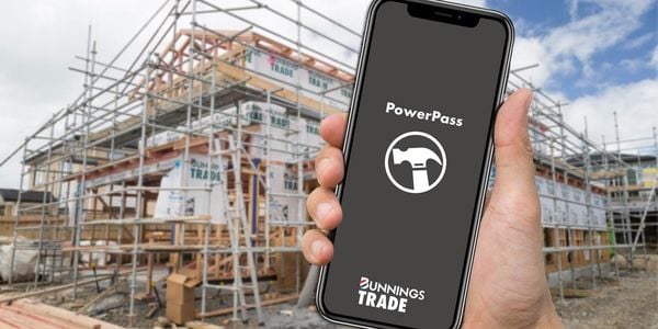 A hand holding a phone with the PowerPass app open on a construction site