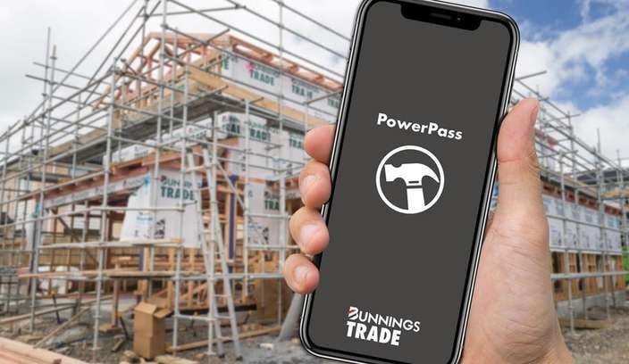 A hand holding a phone with the PowerPass app open on a construction site