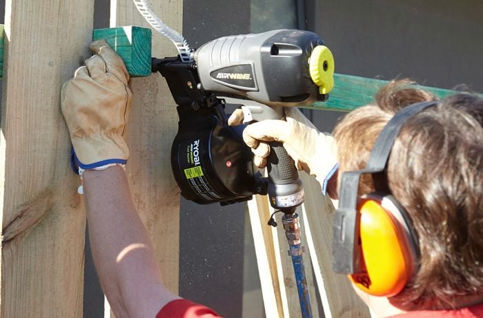 A Bunnings team member nailing a paling to a fence with a nail gun, using a scrap of timber as a spacer between prior palings